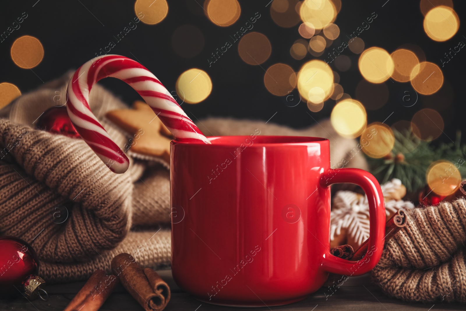 Photo of Cup of tasty cocoa with Christmas candy cane on wooden table against blurred festive lights