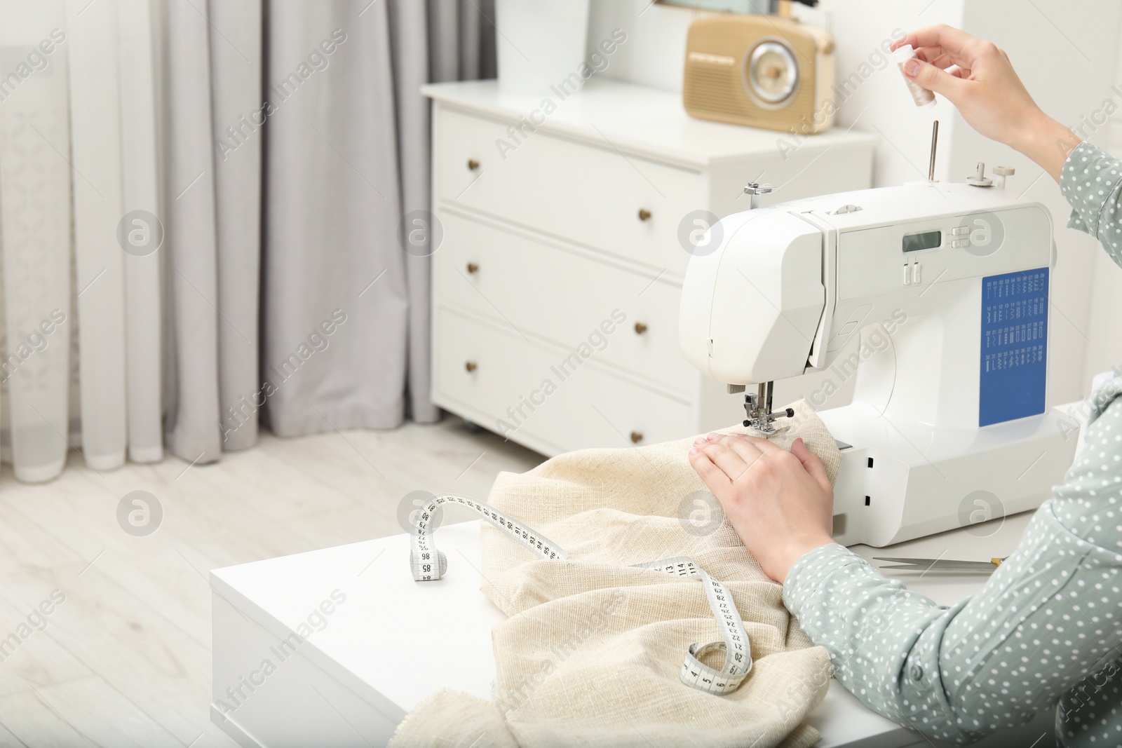 Photo of Seamstress working with sewing machine at table in workshop, closeup. Space for text