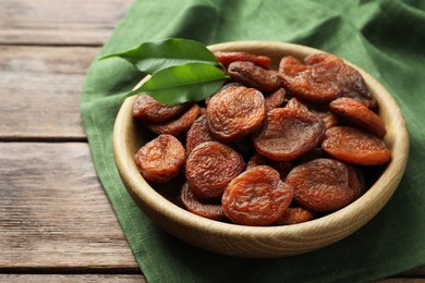 Photo of Bowl of tasty apricots and green leaves on wooden table, closeup. Dried fruits