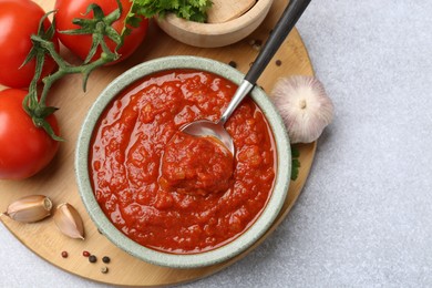 Photo of Homemade tomato sauce in bowl, spoon and fresh ingredients on light grey table, flat lay