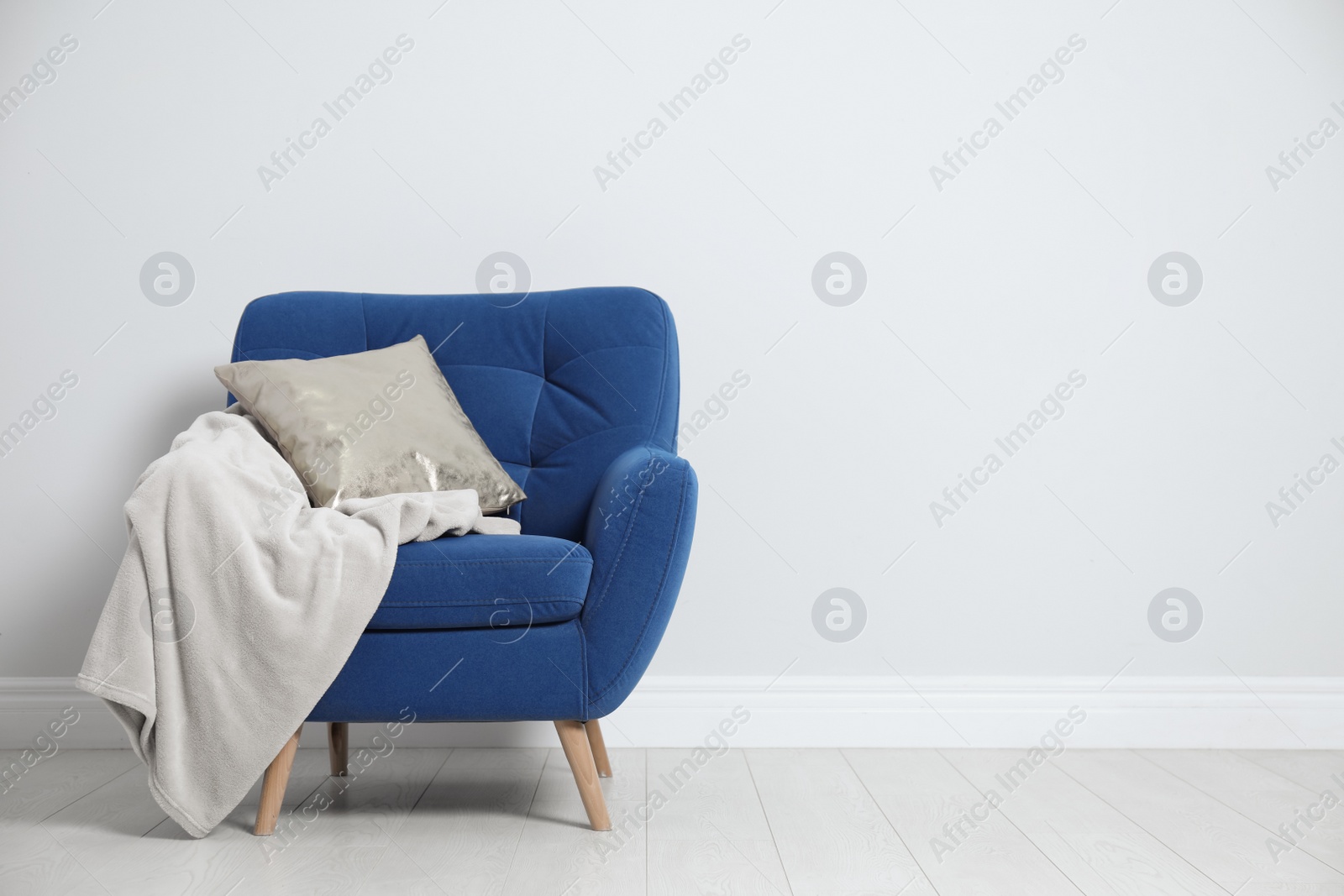 Photo of Stylish armchair with pillow and plaid near white wall, space for text. Interior design