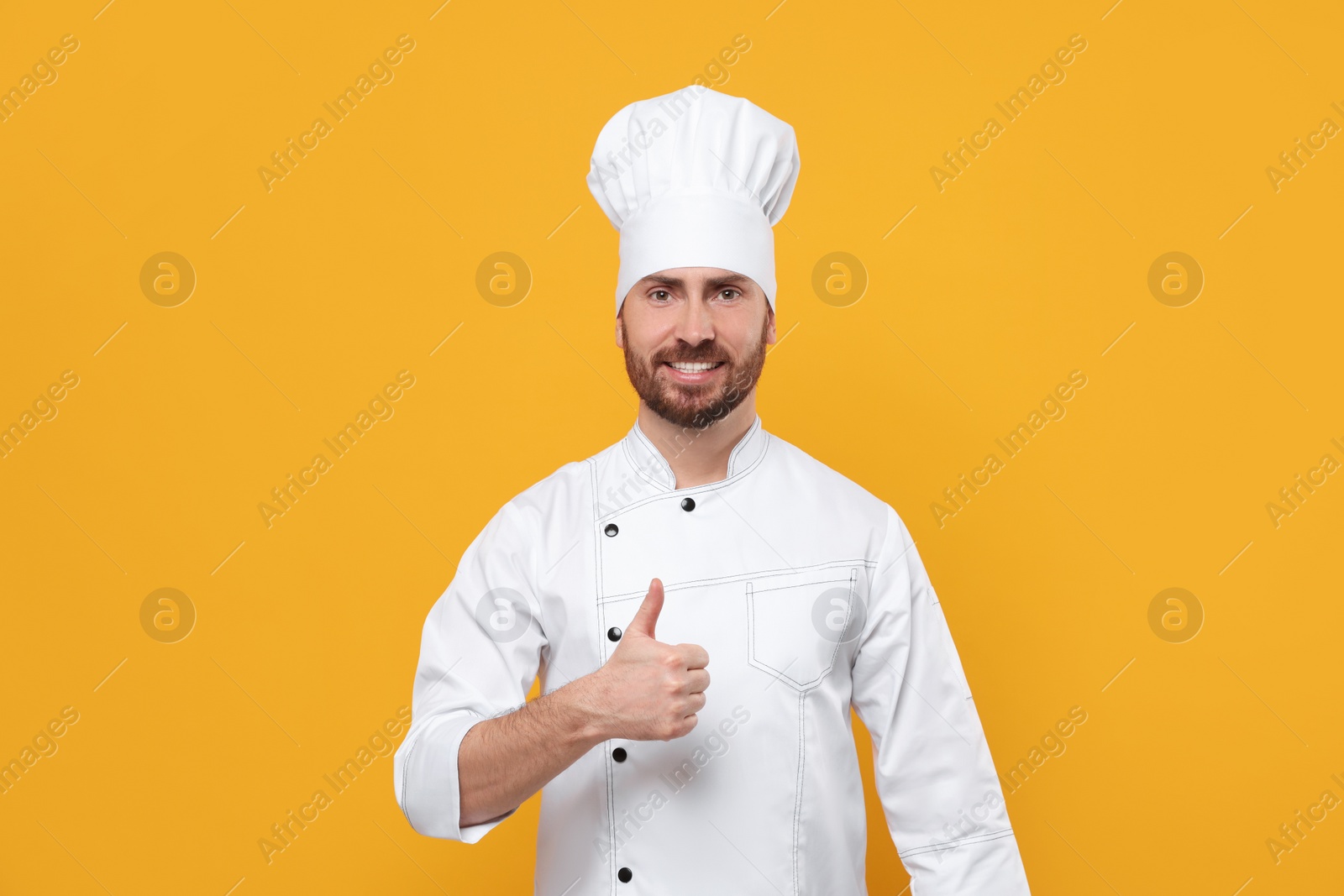 Photo of Smiling mature chef showing thumbs up on orange background