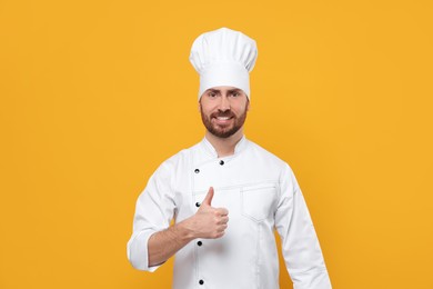 Photo of Smiling mature chef showing thumbs up on orange background