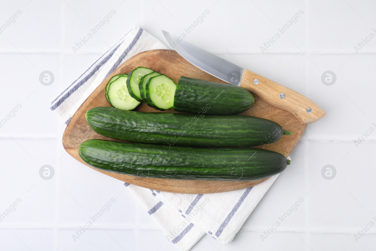 Photo of Fresh cucumbers and knife on white tiled table, top view