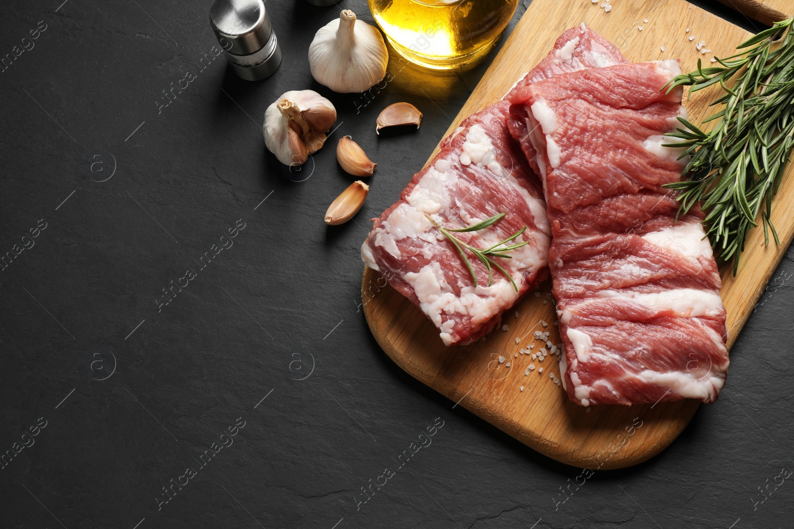 Photo of Raw ribs with rosemary and salt on black table, flat lay. Space for text