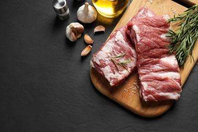 Raw ribs with rosemary and salt on black table, flat lay. Space for text