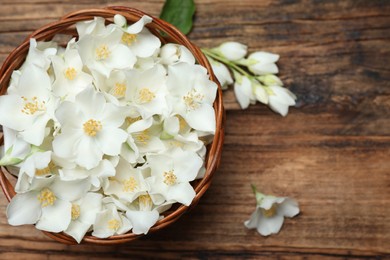 Photo of Beautiful jasmine flowers in wicker bowl on wooden table, top view. Space for text