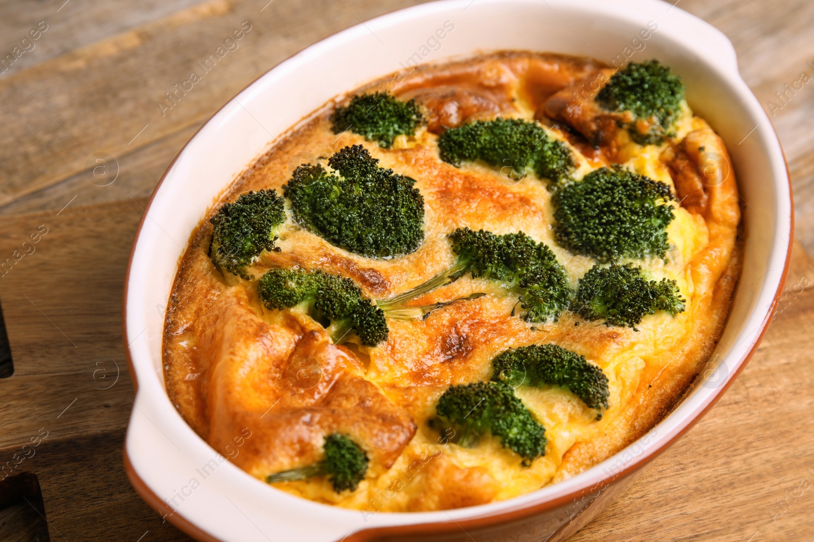 Photo of Tasty broccoli casserole in baking dish on wooden board, closeup