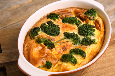 Tasty broccoli casserole in baking dish on wooden board, closeup