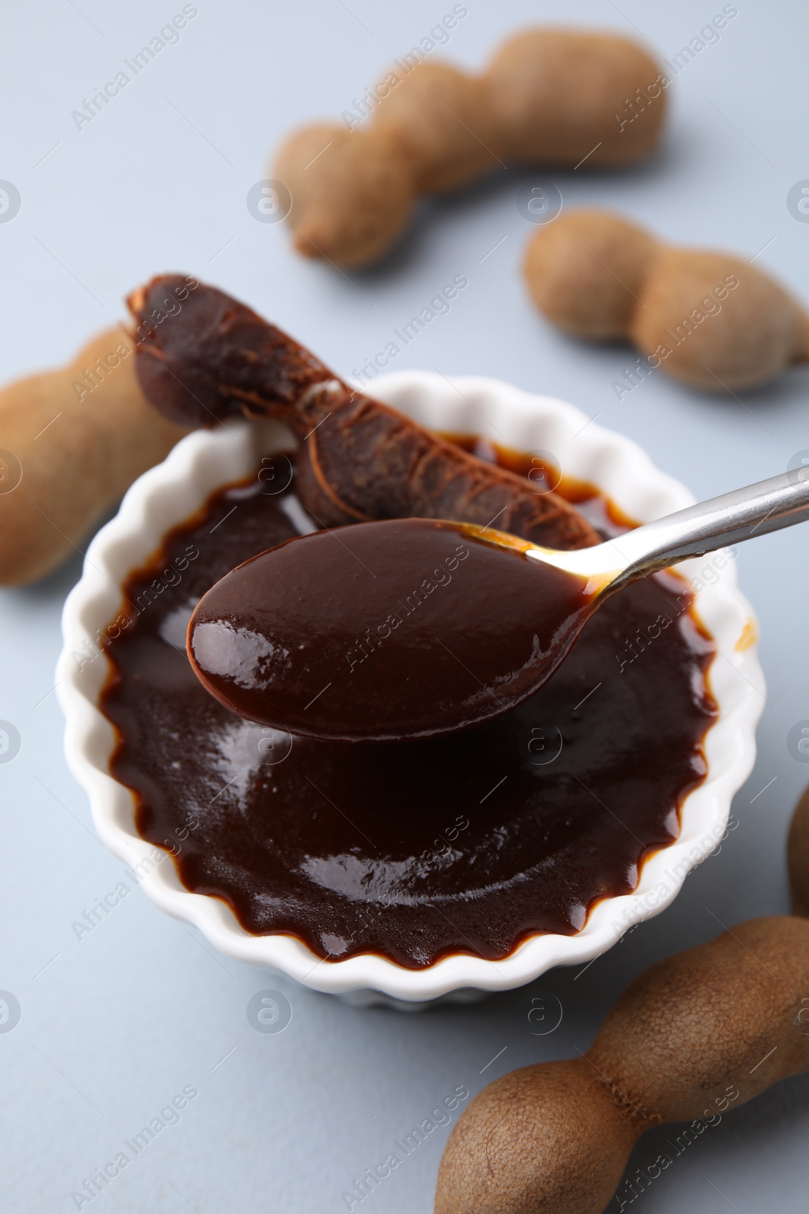 Taking tasty tamarind sauce with spoon from bowl on light grey table Photo of Taking tasty tamarind sauce with spoon from bowl on light grey table
