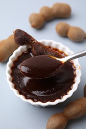 Photo of Taking tasty tamarind sauce with spoon from bowl on light grey table