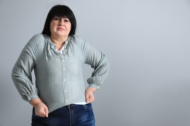 Photo of Overweight woman in tight shirt on light grey background. Space for text