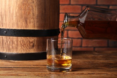 Photo of Pouring whiskey from bottle into glass on wooden table