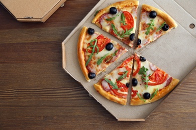 Photo of Cardboard box with tasty pizza on wooden background, top view. Space for text