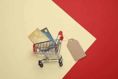 Photo of Shopping cart with credit cards and sale tag on color background, flat lay