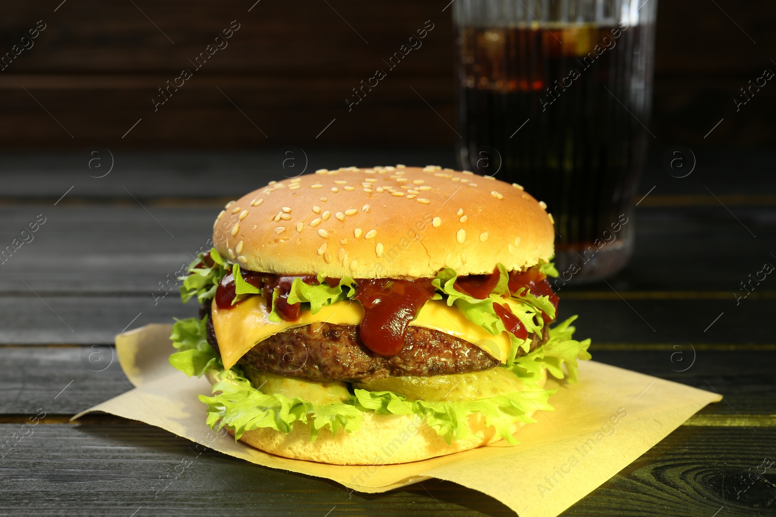 Photo of Burger with delicious patty and soda drink on black wooden table