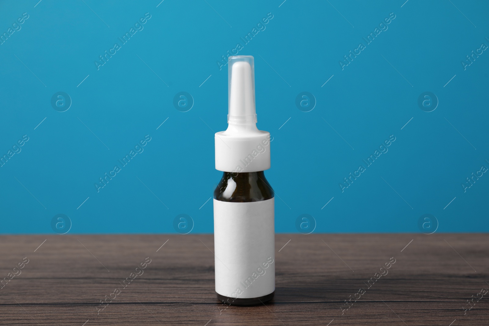 Photo of Nasal spray with blank label on wooden table against light blue background. Space for design