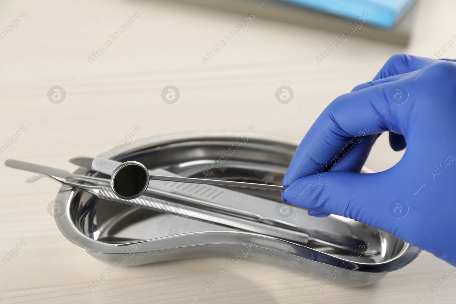 Photo of Dentist taking mouth mirror from kidney shaped tray at wooden table, closeup