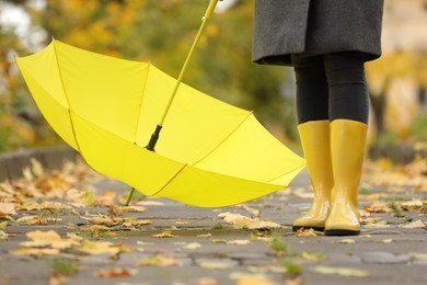 Photo of Woman with yellow umbrella and rubber boots in autumn park, closeup