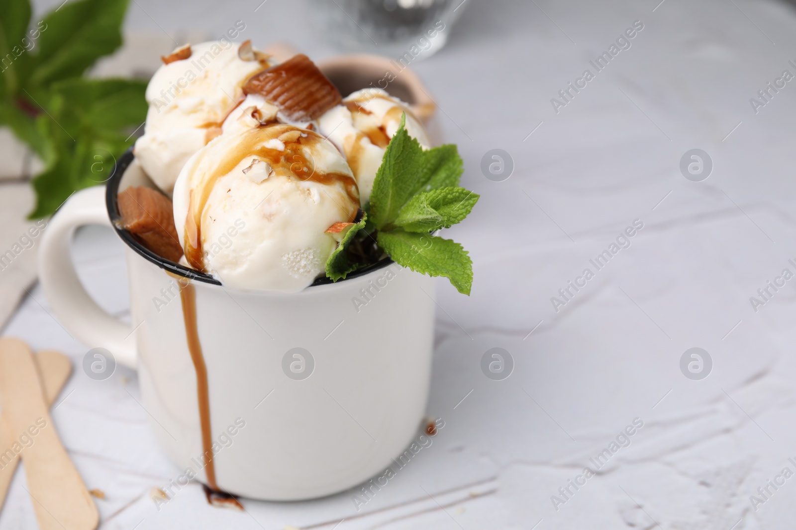 Photo of Scoops of ice cream with caramel sauce, candies and mint leaves on white textured table, closeup. Space for text