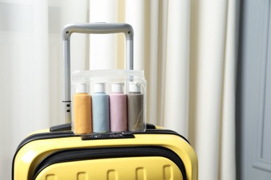 Cosmetic travel kit. Plastic bag with small containers of personal care products on suitcase indoors, space for text