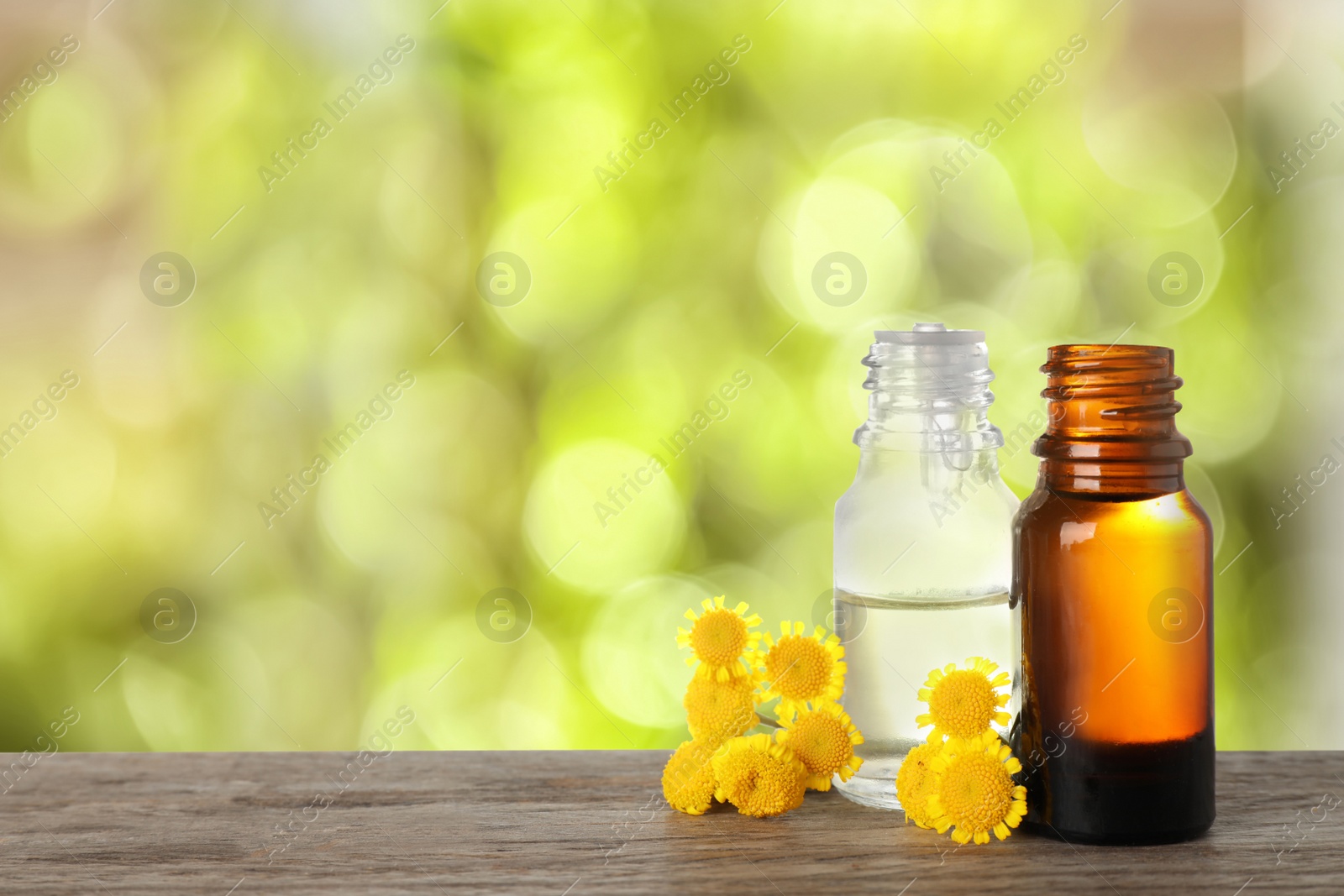 Image of Bottles of essential oil and flowers on wooden table against blurred background. Space for text