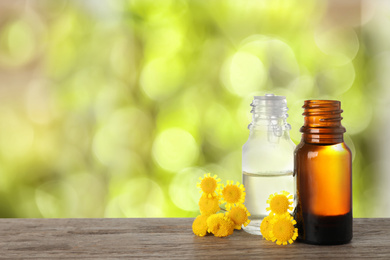 Bottles of essential oil and flowers on wooden table against blurred background. Space for text