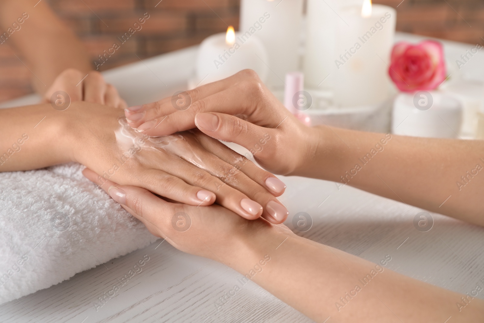 Photo of Cosmetologist applying cream on woman's hand at table in spa salon, closeup