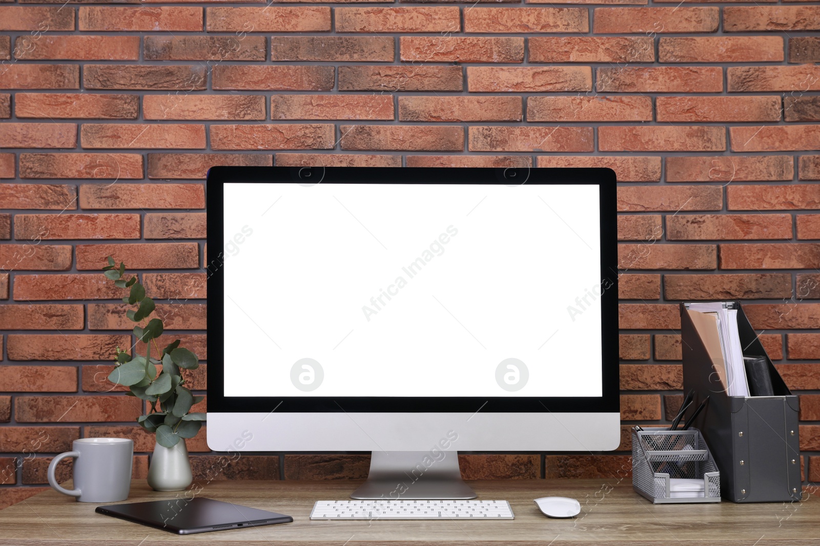 Photo of Modern computer with blank screen on desk near brick wall, space for design. Comfortable workplace