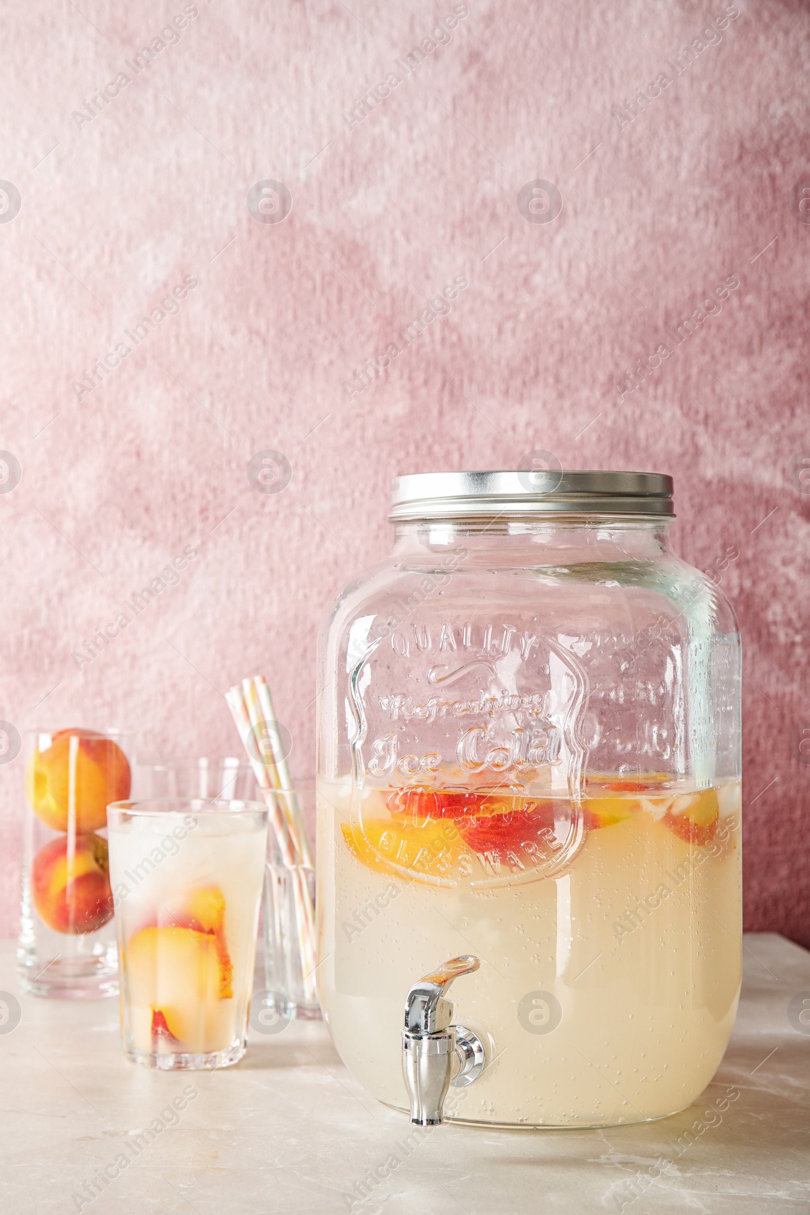 Photo of Peach cocktail in glass and jar with tap on table. Refreshing drink