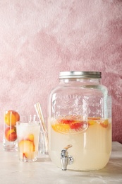 Photo of Peach cocktail in glass and jar with tap on table. Refreshing drink