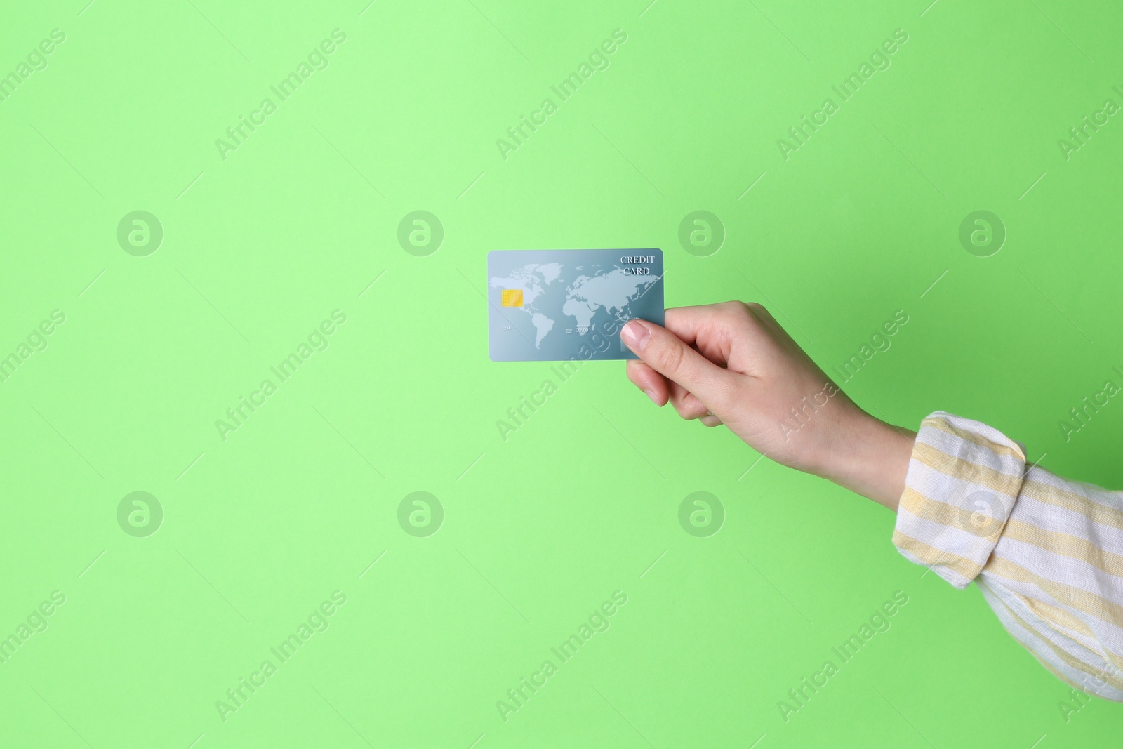 Photo of Woman holding credit card on light green background, closeup