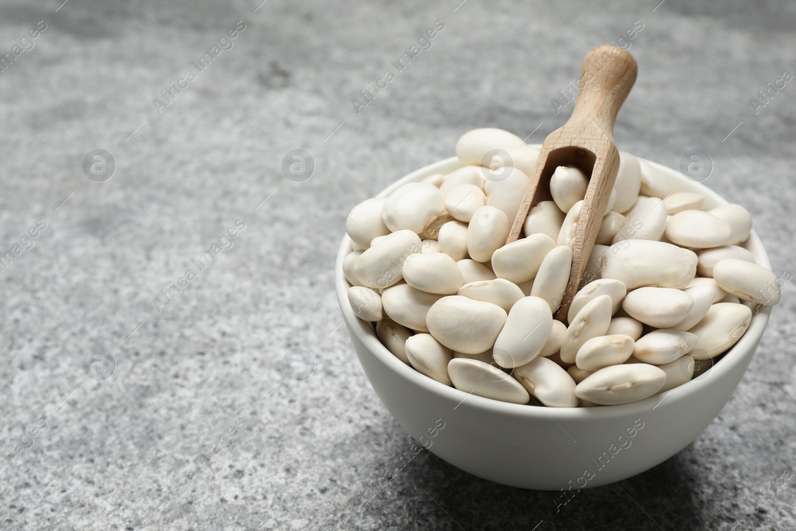 Photo of Raw white beans and scoop in bowl on grey table. Space for text