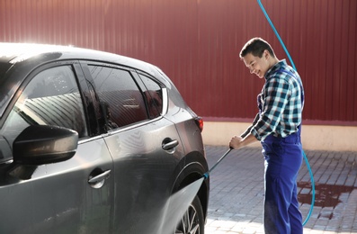 Photo of Worker cleaning automobile with high pressure water jet at car wash