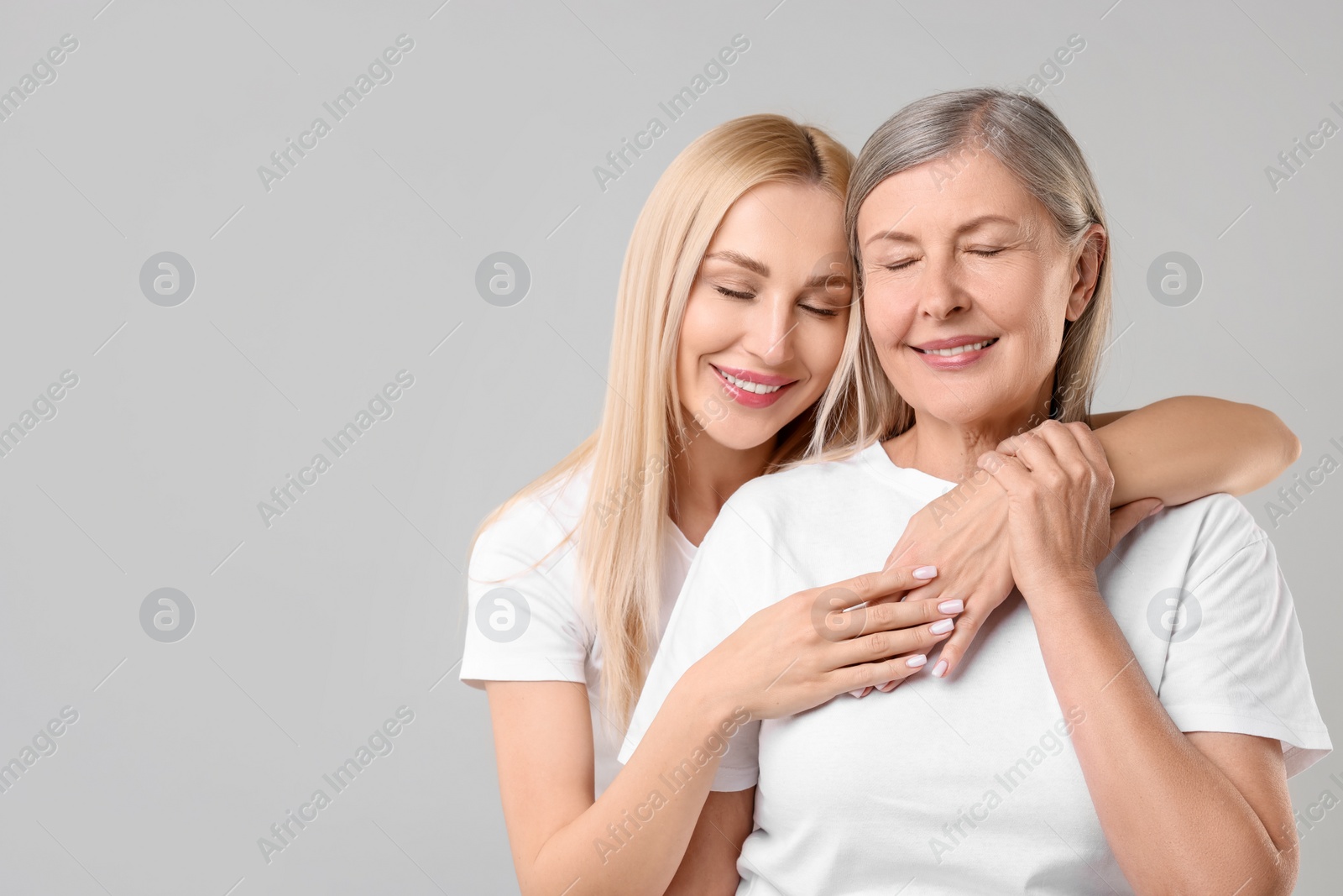 Photo of Family portrait of young woman and her mother on light grey background. Space for text