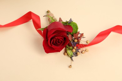 Stylish boutonniere with red rose and ribbon on beige background