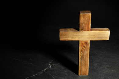 Wooden Christian cross on black slate table against dark background, above view with space for text. Religion concept