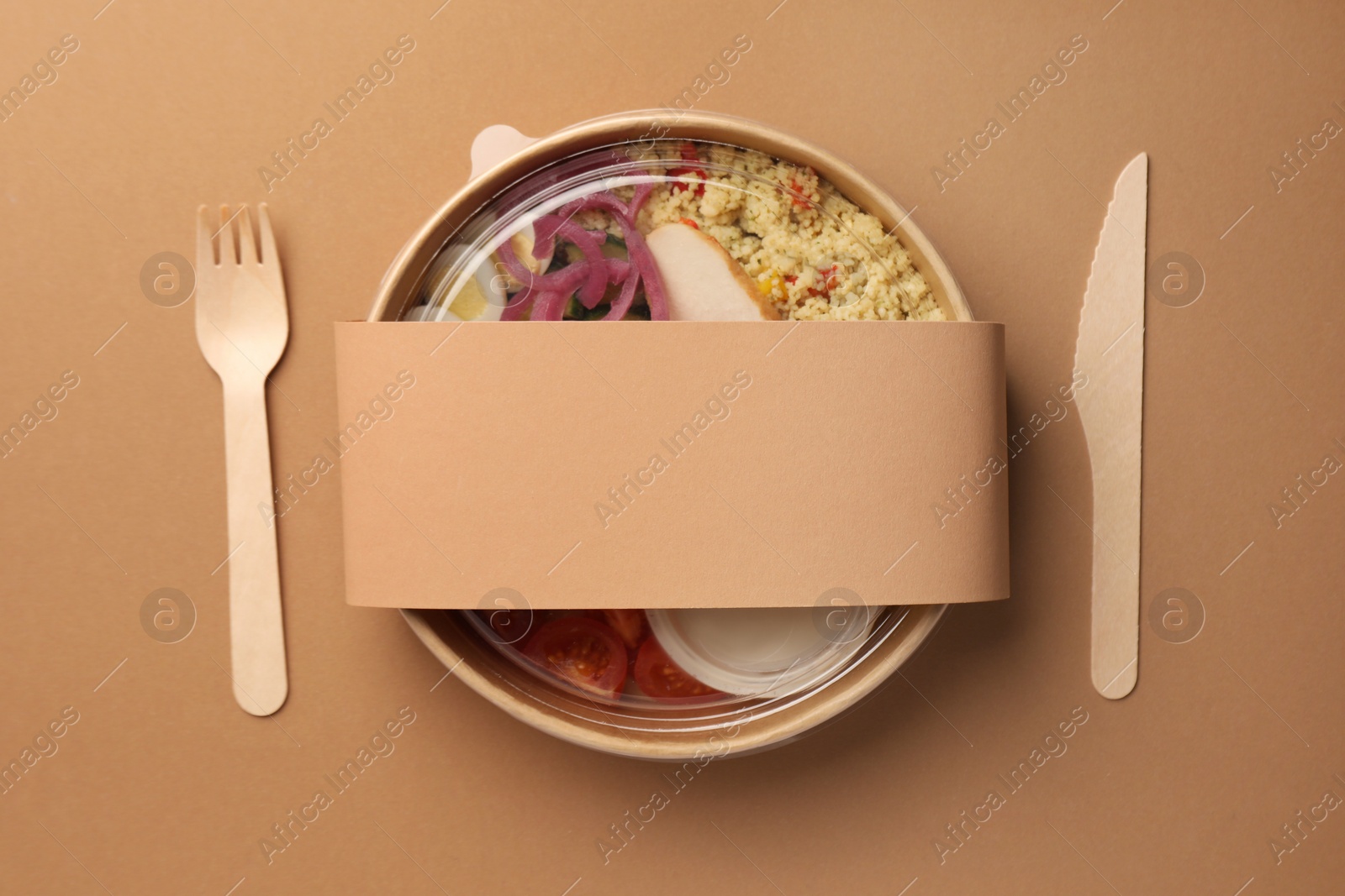 Photo of Tasty food in container with wooden fork and knife on beige background, flat lay. Space for text