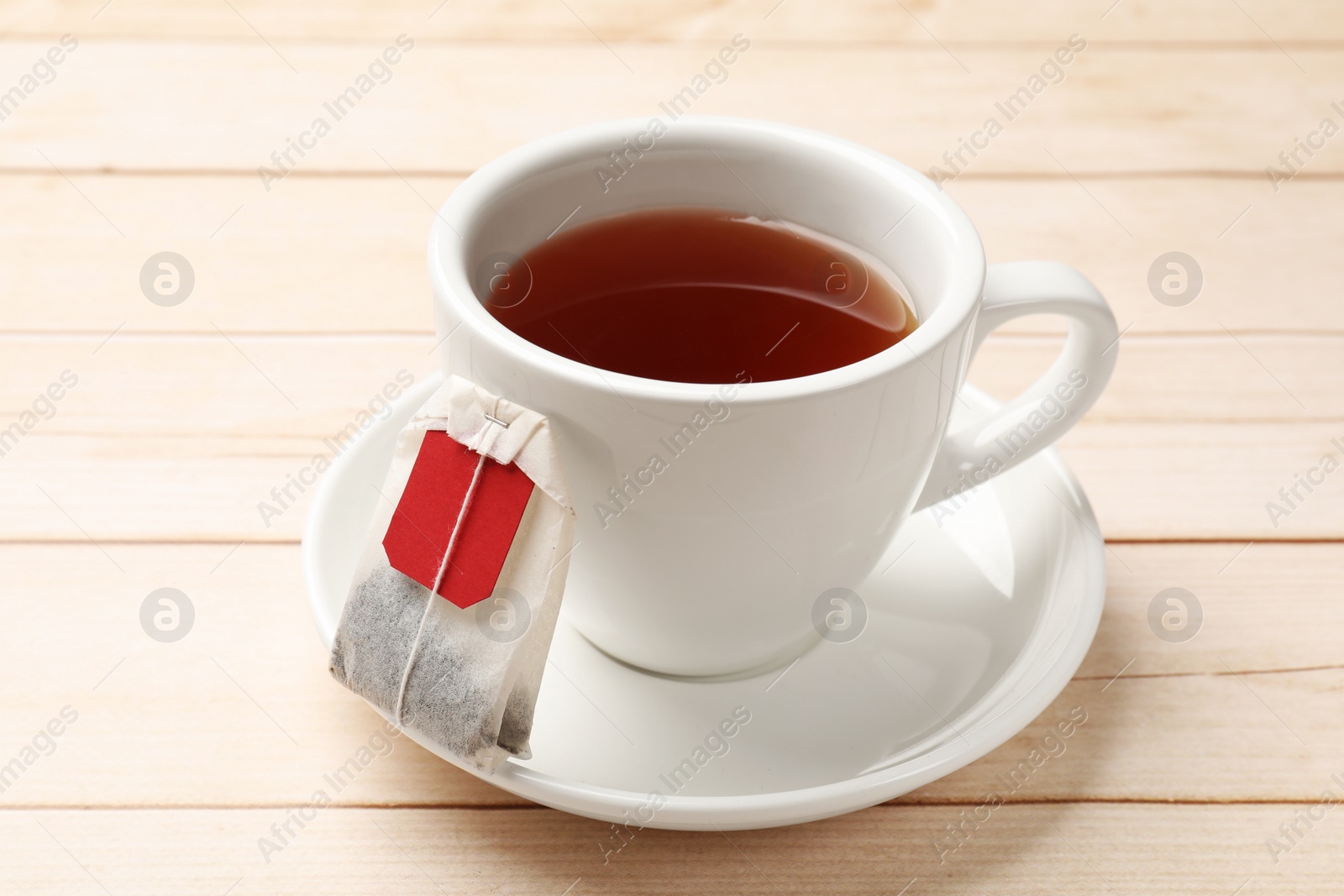 Photo of Tea bag and cup of hot beverage on light wooden table, closeup