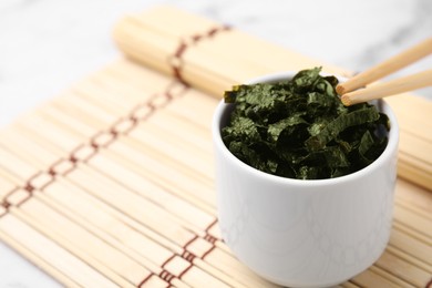 Photo of Chopped nori sheets with chopsticks on white marble table, closeup. Space for text