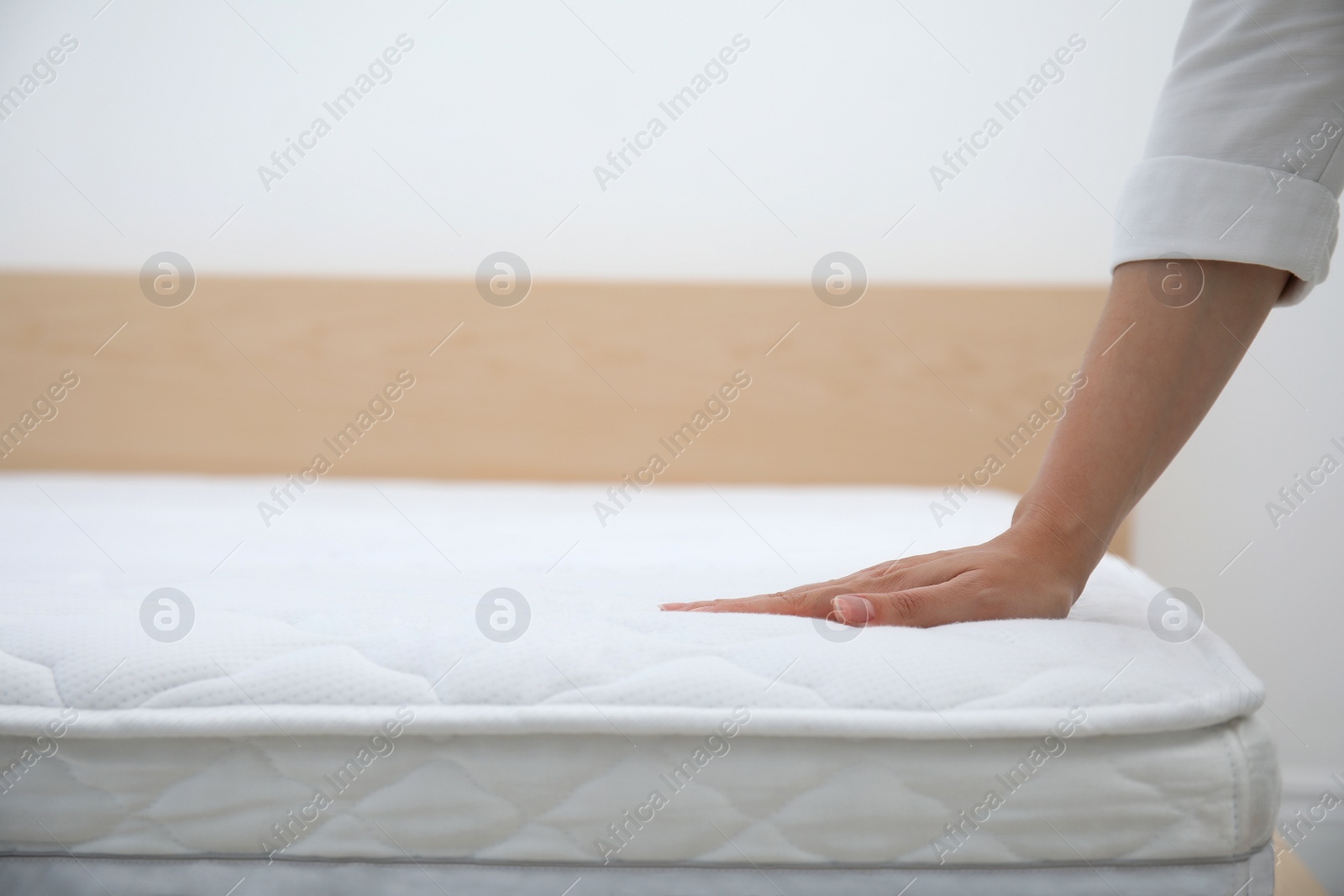 Photo of Woman touching soft white mattress indoors, closeup. Space for text