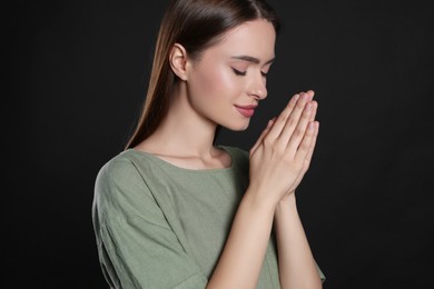 Woman with clasped hands praying on black background