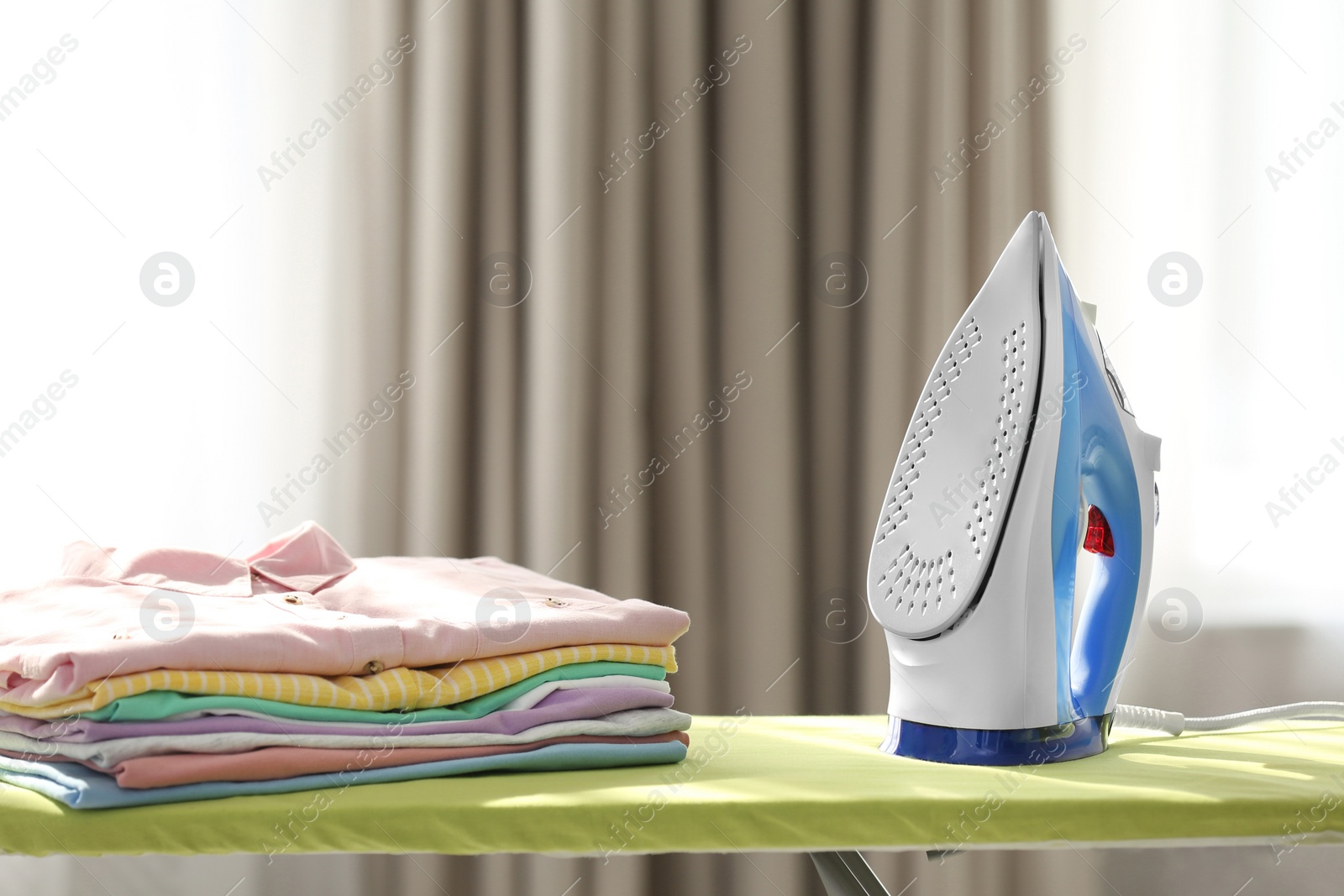 Photo of Board with modern iron and clean laundry at home