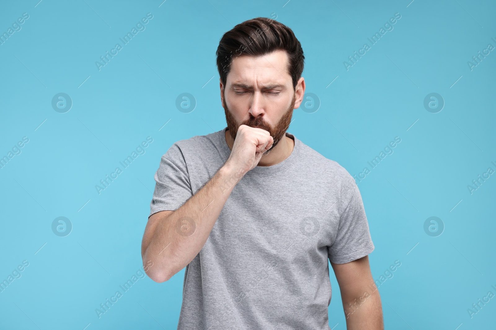 Photo of Sick man coughing on light blue background. Cold symptoms
