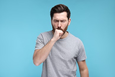 Sick man coughing on light blue background. Cold symptoms