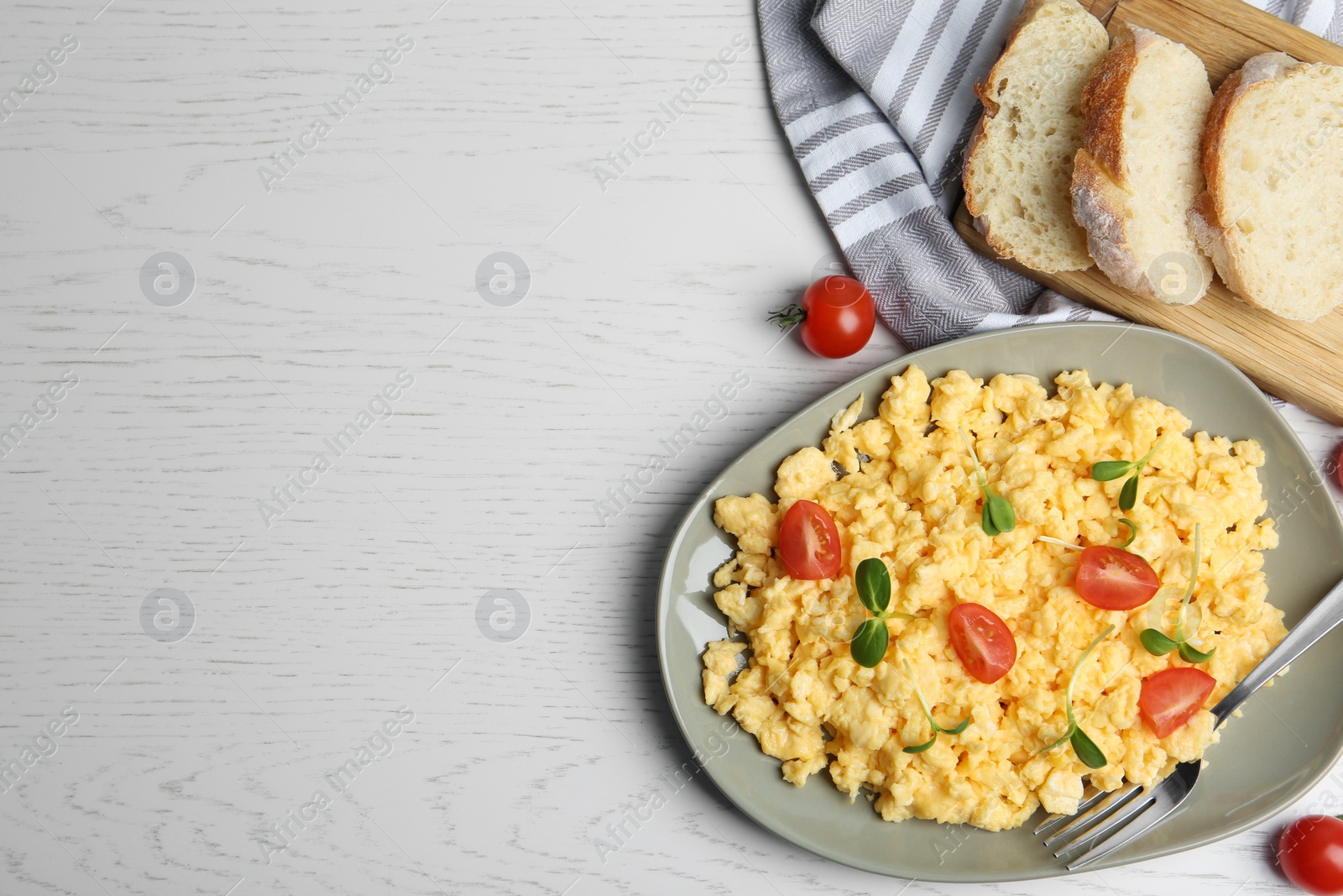 Photo of Tasty scrambled eggs served on white wooden table, flat lay. Space for text