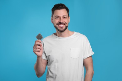 Photo of Happy man holding condom on light blue background