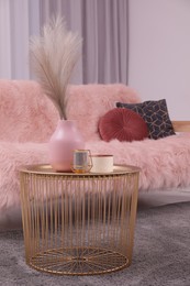 Vase and candles on coffee table near sofa in stylish room. Interior design