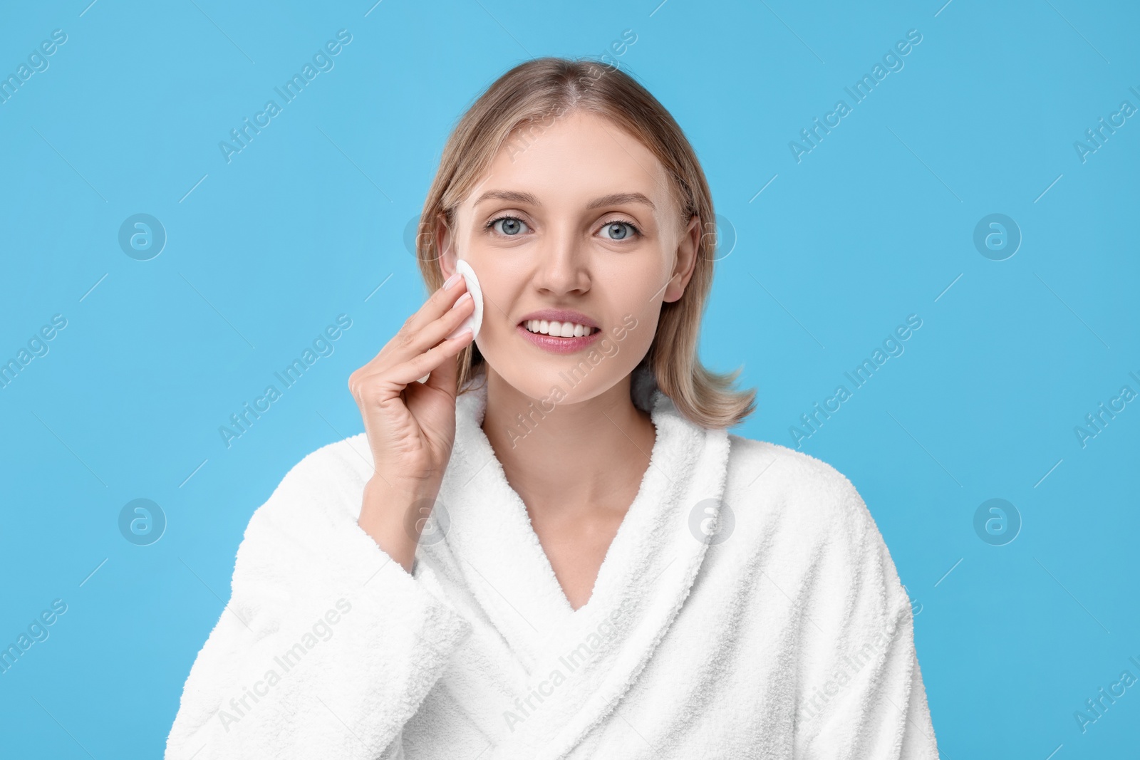 Photo of Young woman cleaning face with cotton pad on light blue background