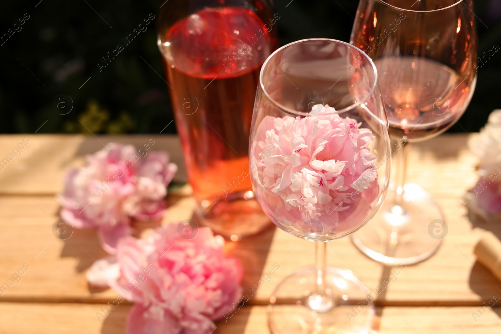 Photo of Bottle and glasses of rose wine near beautiful peonies on wooden table outdoors